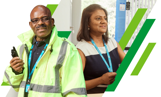 NHS security officer in a high visibility jacket standing next to a woman working on administrative tasks in an office setting.